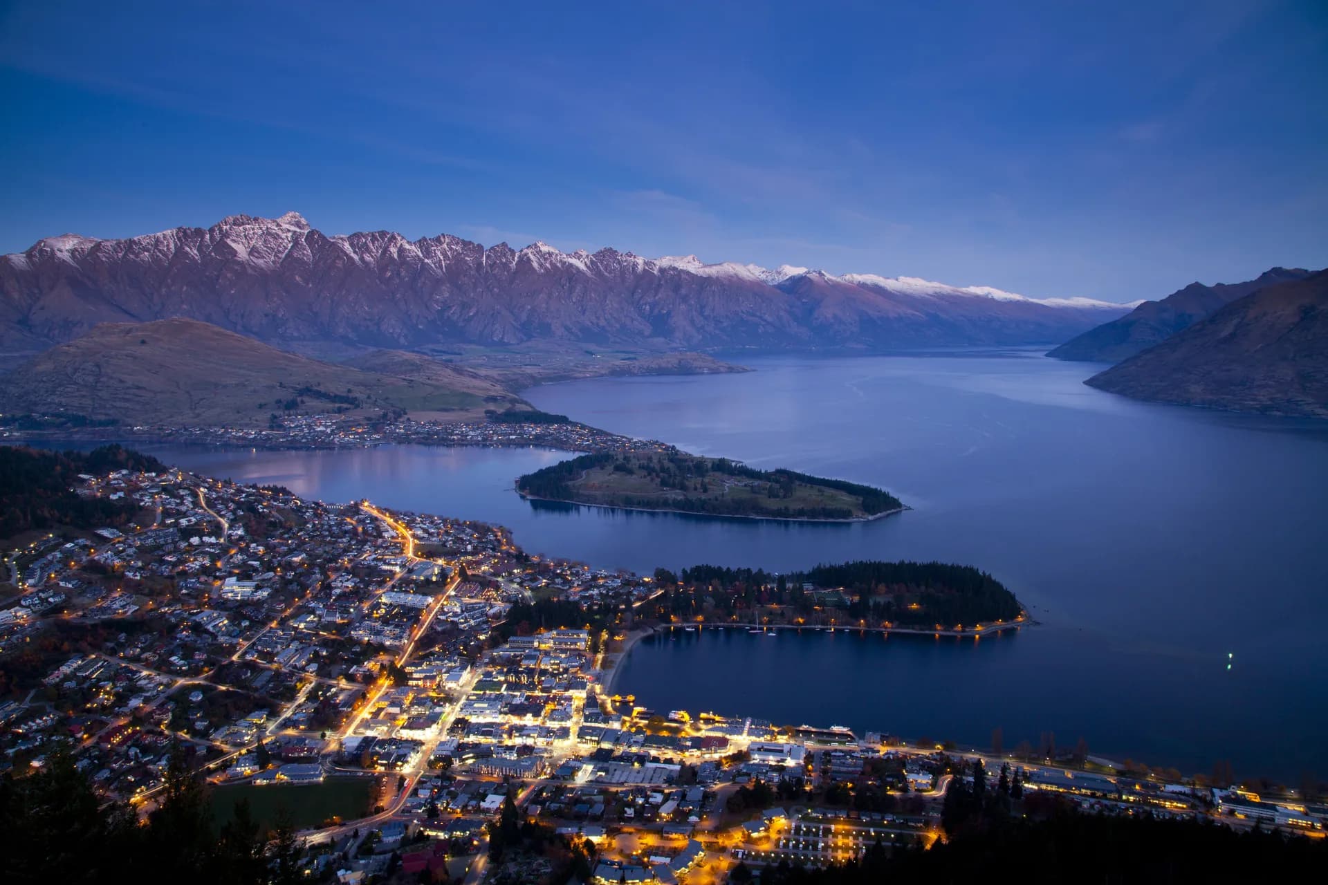 Queenstown from above at dusk, housing climbing the hillside above the lake